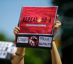 A protester holds a sign outside Queens County Criminal Court Monday, June 8, 2020, calling for the repeal of section 50-a, a law prohibiting the public release of police officer disciplinary records. (AP Photo/Frank Franklin II, File)