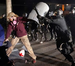 A Portland police officer shoves a protester as police try to disperse the crowd in front of the Multnomah County Sheriff's Office early in the morning on Saturday, Aug. 8, 2020 in Portland, Ore.
