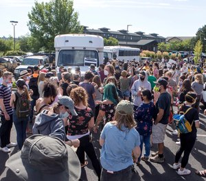 Hundreds of activists gather around two unmarked buses outside the Crane Shed Commons on Wednesday, Aug. 12, 2020, in Bend, Ore.