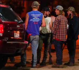 A group holds rifles as they watch protesters on the street Tuesday, Aug. 25, 2020, in Kenosha, Wis. Protests continued following the police shooting of Jacob Blake two days earlier. (AP Photo/Morry Gash)