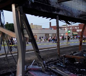 Protesters march past a burned out building damaged in protests against the Sunday police shooting of Jacob Blake in Kenosha, Wis., Wednesday, Aug. 26, 2020.