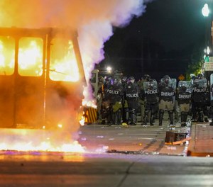 In this Aug. 24, 2020 file photo, police stand near a garbage truck ablaze during protests over the shooting of Jacob Blake in Kenosha, Wis.