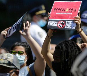 In this June 8, 2020 file photo, a protester holds a sign outside Queens County Criminal Court calling for the repeal of section 50-a, a law prohibiting the public release of police officer disciplinary records. (AP Photo/Frank Franklin II, File)