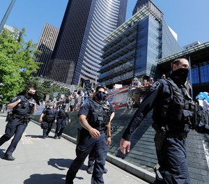 In this Wednesday, July 15, 2020, file photo, Seattle Police officers walk past people holding signs and flags during a rally in support of police in front of City Hall in Seattle. (AP Photo/Ted S. Warren, File)