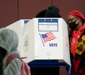 A woman helps a man cast his ballot in person on the last day of early voting, Sunday, Nov. 1, 2020, at P.S. 175 in the Harlem neighborhood of New York.