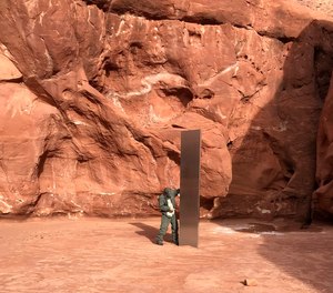 A Utah state worker inspects a metal monolith that was found installed in the ground in a remote area of red rock in Utah.