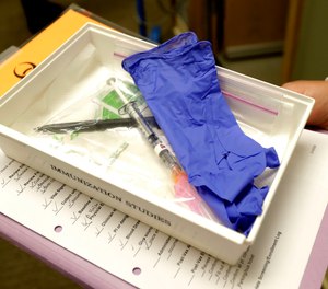 In this March 16, 2020, file photo, pharmacist Michael Witte holds a tray with a syringe containing a shot that will be used in the first clinical trial of a potential vaccine for COVID-19 at the Kaiser Permanente Washington Health Research Institute in Seattle. The Advisory Committee on Immunization Practices has voted to put healthcare workers, including EMS providers, and residents at long-term care facilities in the first priority group for the COVID-19 vaccine.