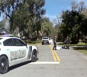 In this Feb. 23, 2020 image taken from Glynn, Ga., County Police body camera video, authorities, rear, stand over the covered body of Ahmaud Arbery.