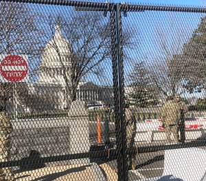 Members of the National Guard stand inside anti-scaling fencing that surrounds the Capitol, Sunday, Jan. 10, 2021, in Washington.