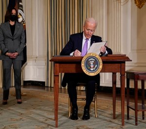 President Joe Biden signs executive orders in the State Dining Room of the White House, Tuesday, Jan. 26, 2021, in Washington. Vice President Kamala Harris listens at left.