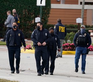 Law enforcement officers walk near the entrance to an apartment complex where a shooting wounded several FBI agents while serving an arrest warrant, Tuesday, Feb. 2, 2021, in Sunrise, Fla.