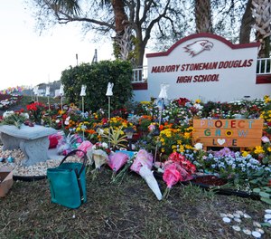 In this Feb. 14, 2019, file photo, Suzanne Devine Clark, an art teacher at Deerfield Beach Elementary School, places painted stones at a memorial outside Marjory Stoneman Douglas High School during the firstr anniversary of the school shooting in Parkland, Fla.