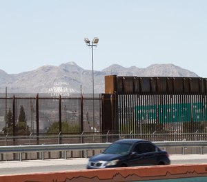 A car drives on a highway parallel to a border fence in El Paso, Texas.