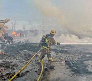 A firefighter battles a fire at at commercial yard in Compton, Calif., on Friday, Feb. 26, 2021. A huge fire visible across Los Angeles burned material in a commercial yard and parked buses early Friday.