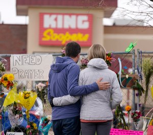 Mourners walk the temporary fence line outside the parking lot of a King Soopers grocery store, the site of a mass shooting in which 10 people died, Friday, March 26, 2021, in Boulder, Colo.