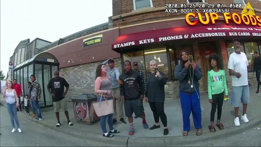 Firefighter Genevieve Hansen is pictured in this police body cam video (center, all black clothing) filming on her cell phone as onlookers begged Minneapolis Officer Derek Chauvin to take his knee off George Floyd’s neck.