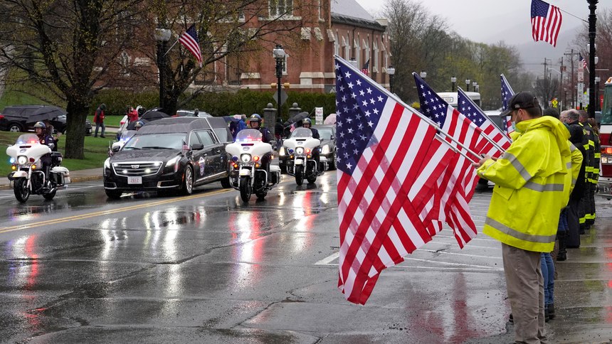 A hearse carrying the coffin of the late U.S. Capitol Police officer William "Billy" Evans, left, drives past people holding flags while escorted by motorcycles though Adams, Mass., following a funeral Mass for Evans, Thursday, April 15, 2021.