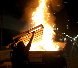 Protesters light a fire in a dumpster in downtown Portland, Ore., Friday, April 16, 2021.