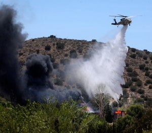 A firefighting helicopter makes a water drop on a house engulfed in fire following a shooting at LACoFD Fire Station 81.