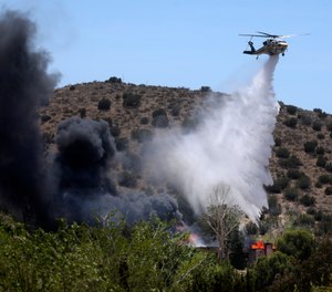 A firefighting helicopter makes a water drop on a house engulfed in fire following a shooting at LACoFD Fire Station 81.