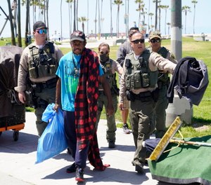 Members of the Los Angeles County Sheriffs Department's HOST, Homeless Outreach Service Team, walk with a homeless man in the Venice Beach section of Los Angeles.