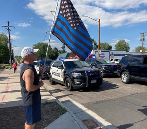 A man holds a blue line flag at the beginning of a line of about 30 police cars lined up for a procession in honor of the officer who was fatally shot in Arvada, Colo., on Monday, June 21, 2021.