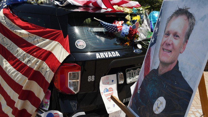 Flowers, flags and notes cover a patrol car and bike outside Arvada City Hall during a memorial for Arvada Police Officer Gordon Beesley on Tuesday, June 22, 2021 in Arvada, Colo. Officer Beesley was killed during a shooting in Olde Town Arvada. 