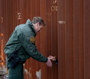 In this Jan 15, 2019, file photo, Rodney Scott, then-U.S. Border Patrol's San Diego sector chief shakes hands through a section of newly-replaced border wall in San Diego.