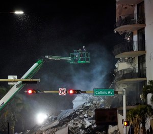 Workers ride in a lift as smoke rises off the rubble where a wing of a 12-story beachfront condo building collapsed, late on Thursday, June 24, 2021, in the Surfside area of Miami.