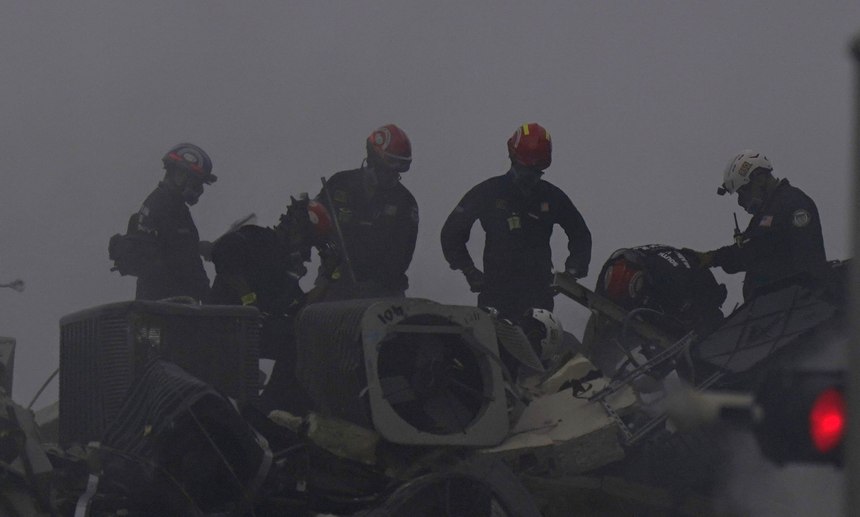 Search and rescue personnel search for survivors through the rubble at the Champlain Towers South Condo as thick smoke from a fire within the rubble fills the air.