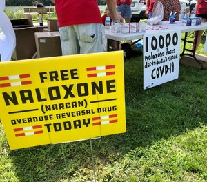Signs are displayed at a tent during a health event on June 26, 2021, in Charleston, W.Va. Volunteers at the tent passed free doses of naloxone, a drug that reverses the effects of an opioid overdose by helping the person breathe again.