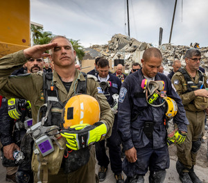 A member of the Israeli search and rescue team, left, salutes in front of the rubble that once was Champlain Towers South during a prayer ceremony, Wednesday, July 7, 2021, in Surfside, Fla. Members of search and rescue teams and Miami-Dade Fire rescue, along with police and workers who have been working at the site of the collapse gathered for a moment of prayer and silence next to the collapsed tower.
