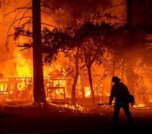 A firefighter passes a burning home as the Dixie Fire flares in Plumas County, Calif.