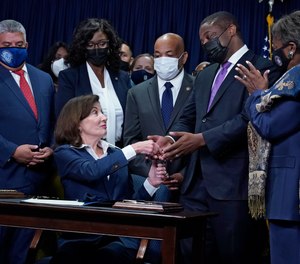 New York Gov. Kathy Hochul, seated, hands the first pen, during the signing of the