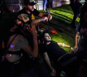 In this Aug. 25, 2020 file photo, Gaige Grosskreutz (top) tends to an injured protester during clashes with police outside the Kenosha County Courthouse in Kenosha, Wis.