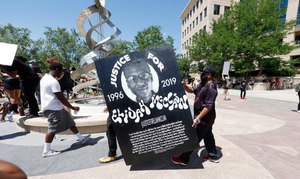 In this June 27, 2020, file photo, demonstrators carry a giant placard during a rally and march over the death of 23-year-old Elijah McClain outside the police department in Aurora, Colo.