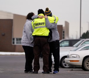 An Oakland County Sheriff's deputy hugs a student's family members in the parking lot of Oxford High School in Oxford, Mich., Wednesday, Dec. 1, 2021. A 15-year-old sophomore opened fire at the school, killing several students and wounding multiple others.