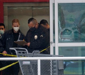 Police officers work near a broken glass door at the scene where two people were struck by gunfire in a police shooting at a Burlington Coat Factory store in North Hollywood, Calif., Thursday, Dec. 23, 2021.