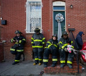Firefighters stand in a line near an ambulance after a firefighter who died while battling a two-alarm fire in a vacant row home was pulled from the collapsed building.