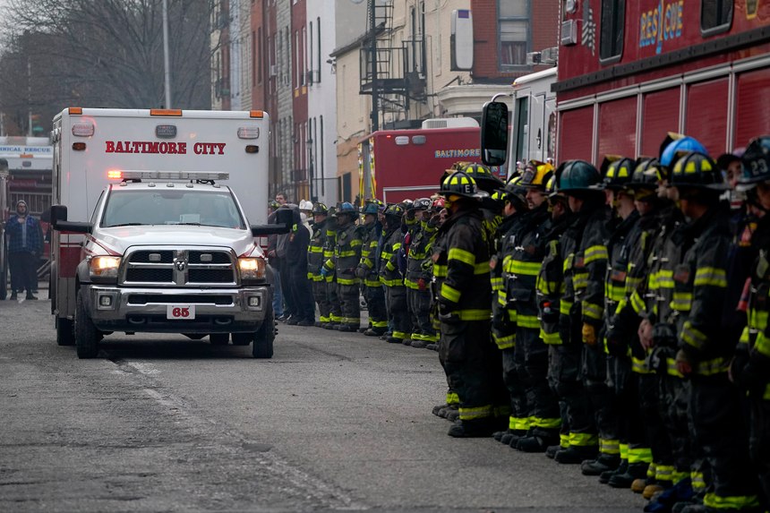 Firefighters salute as an ambulance carries a deceased firefighter after they were pulled out of a collapsed building while battling a two-alarm fire at a vacant row home, Monday, Jan. 24, 2022, in Baltimore. Officials said several firefighters died during the blaze.