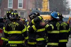 Firefighters embrace each other after a deceased firefighter was pulled out of a building collapse while battling a two-alarm fire in a vacant row home, Monday, Jan. 24, 2022, in Baltimore. Officials said several firefighters died during the blaze.