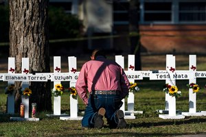 Pastor Daniel Myers kneels in front of crosses bearing the names of Tuesday's shooting victims while praying for them at Robb Elementary School in Uvalde, Texas, on Thursday.