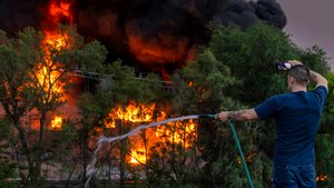 A man sprays down the roof of a neighboring building while also filming a three-alarm fire at Nox-Crete, Inc. on Monday.