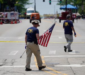 A member of the FBI's evidence response team removes an American flag one day after a mass shooting in downtown Highland Park, Ill., Tuesday, July 5, 2022.