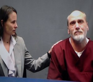 In this photo from a video screen, death row inmate James Coddington, right, speaks to the Oklahoma Board of Pardon and Parole Wednesday, Aug. 3, 2022, in Oklahoma City. Julie Gardner, investigator at the Oklahoma Federal Defenders Office, is at left. An emotional Coddington apologized to the victim's family and said he is