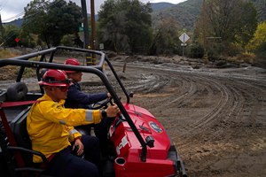 Emergency crews ride along a mud-covered road in the aftermath of a mudslide Tuesday in Oak Glen, Calif. Cleanup efforts and damage assessments are underway east of Los Angeles after heavy rains unleashed mudslides in a mountain area scorched by a wildfire two years ago.