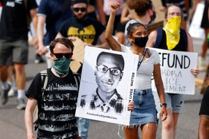 A demonstrator carries an image of Elijah McClain during a rally and march in Aurora, Colo., on June 27, 2020. A Colorado judge on Friday responded to a request by a coalition of news organizations to release an amended autopsy report for McClain, a 23-year-old Black man who died after a 2019 encounter with police, by ruling the report be made public only after new information it contains is redacted.
