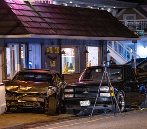 A sedan is wedged between a small, black pickup truck and the Bagel Time Cafe in Wildwood, N.J., early Sunday, Sept. 25, 2022. Authorities say at least two people were killed amid multiple crashes at a pop-up car rally.