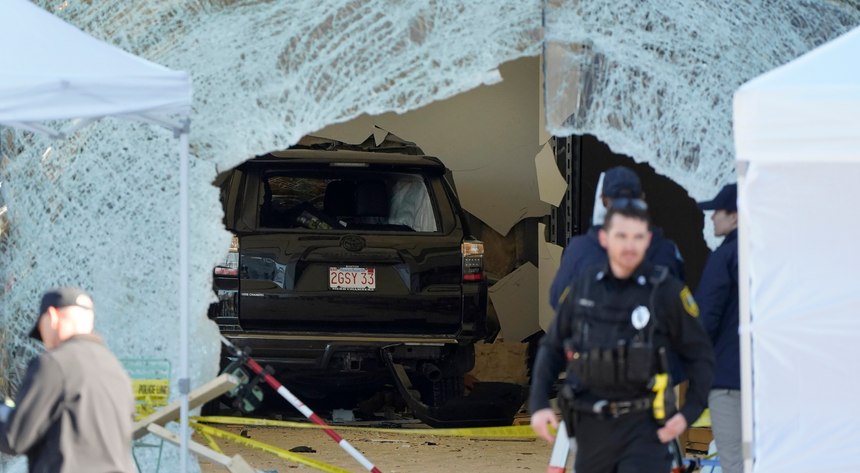 An SUV rests inside an Apple store behind a large hole in the glass front of the store in Hingham, Mass.