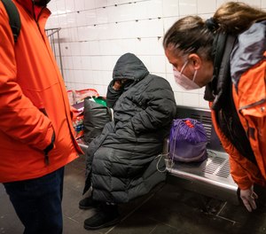 Homeless Outreach personnel reach out to a person sleeping on a bench in the Manhattan subway system, Monday, Feb. 21, 2022, in New York.